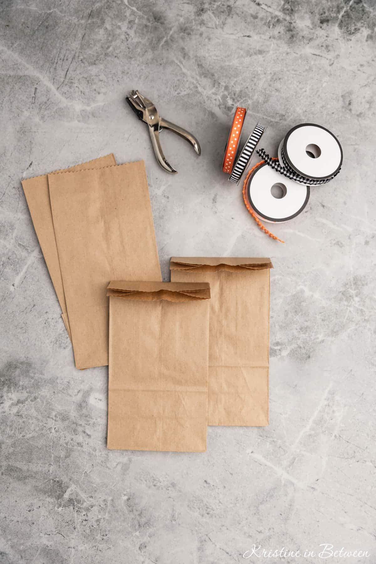 Brown paper bags with cut off edges folded down laying with ribbon and a hole punch.