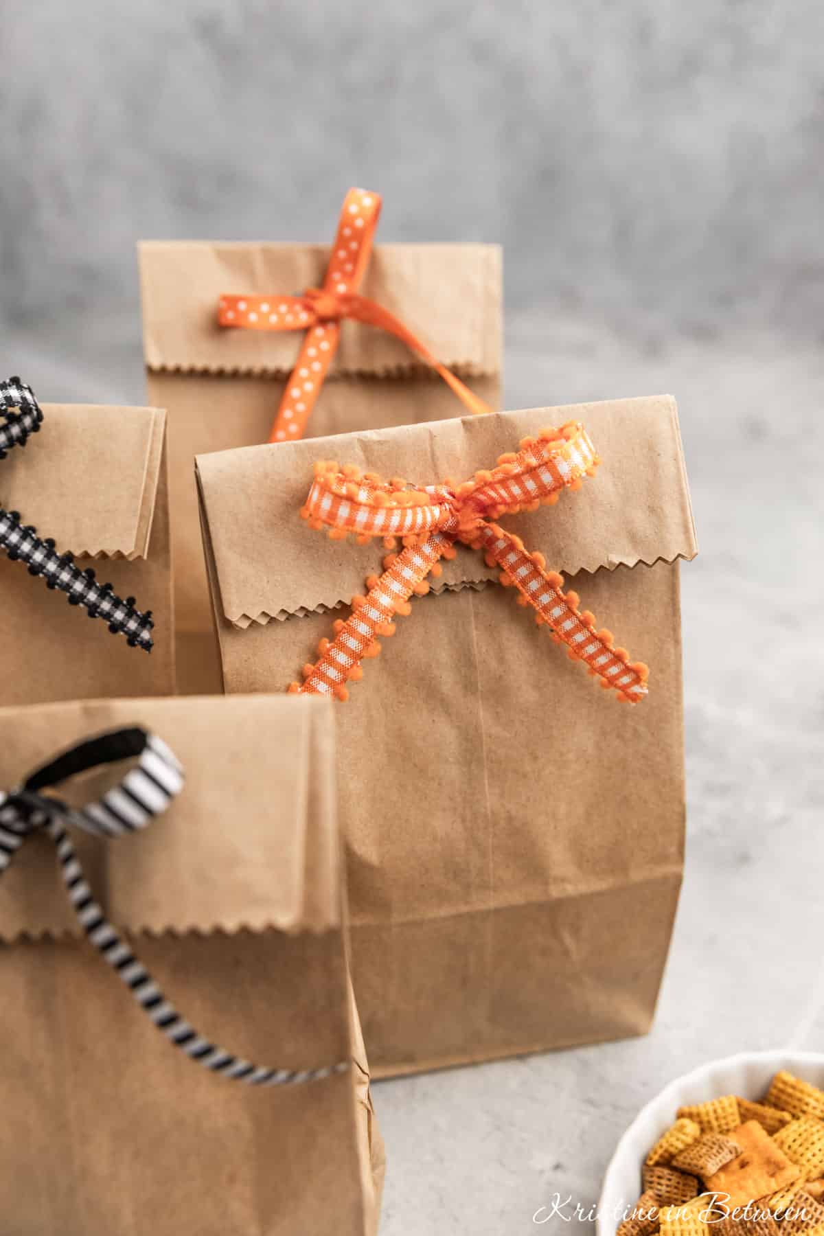 Halloween treat bags made out of brown paper bags sitting with a small bowl of snack mix.
