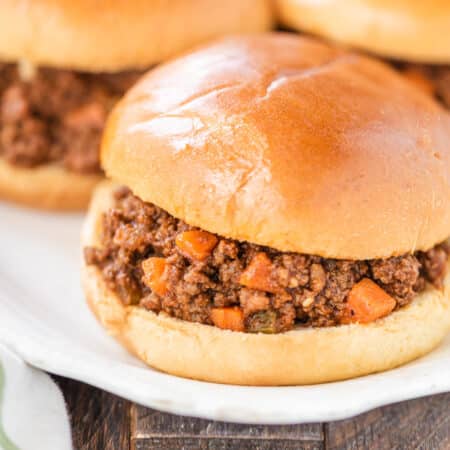 A Sloppy Joe sitting on a white plate with a few more in the background.