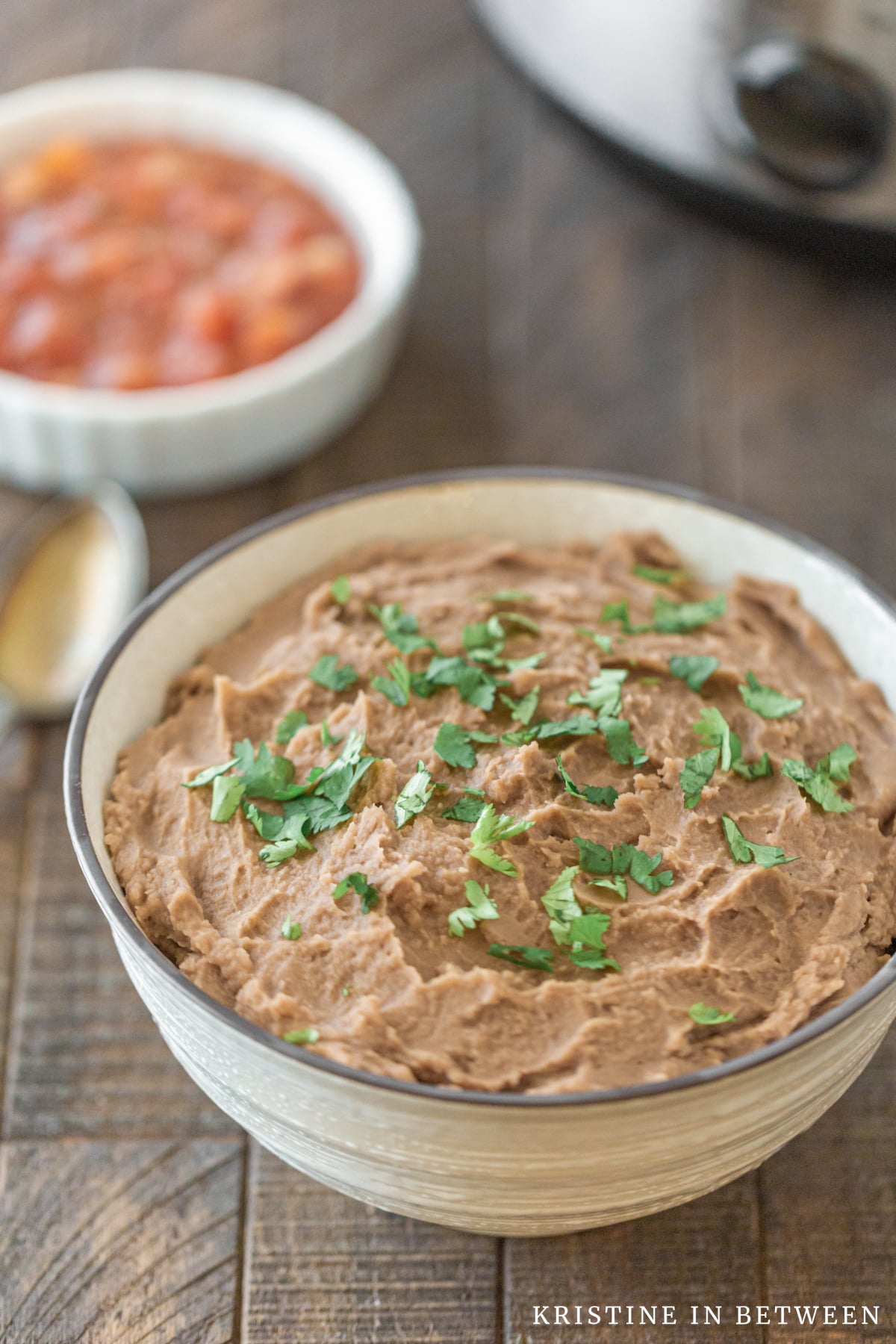A bowl of refried beans sitting next to a Crock-pot and a small bowl of salsa.