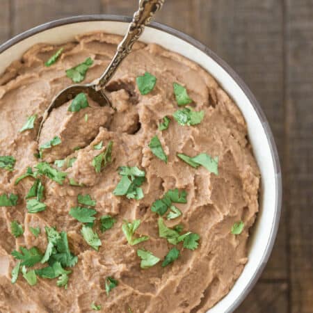 A bowl of refried beans sitting next to a Crock-pot and a small bowl of salsa.