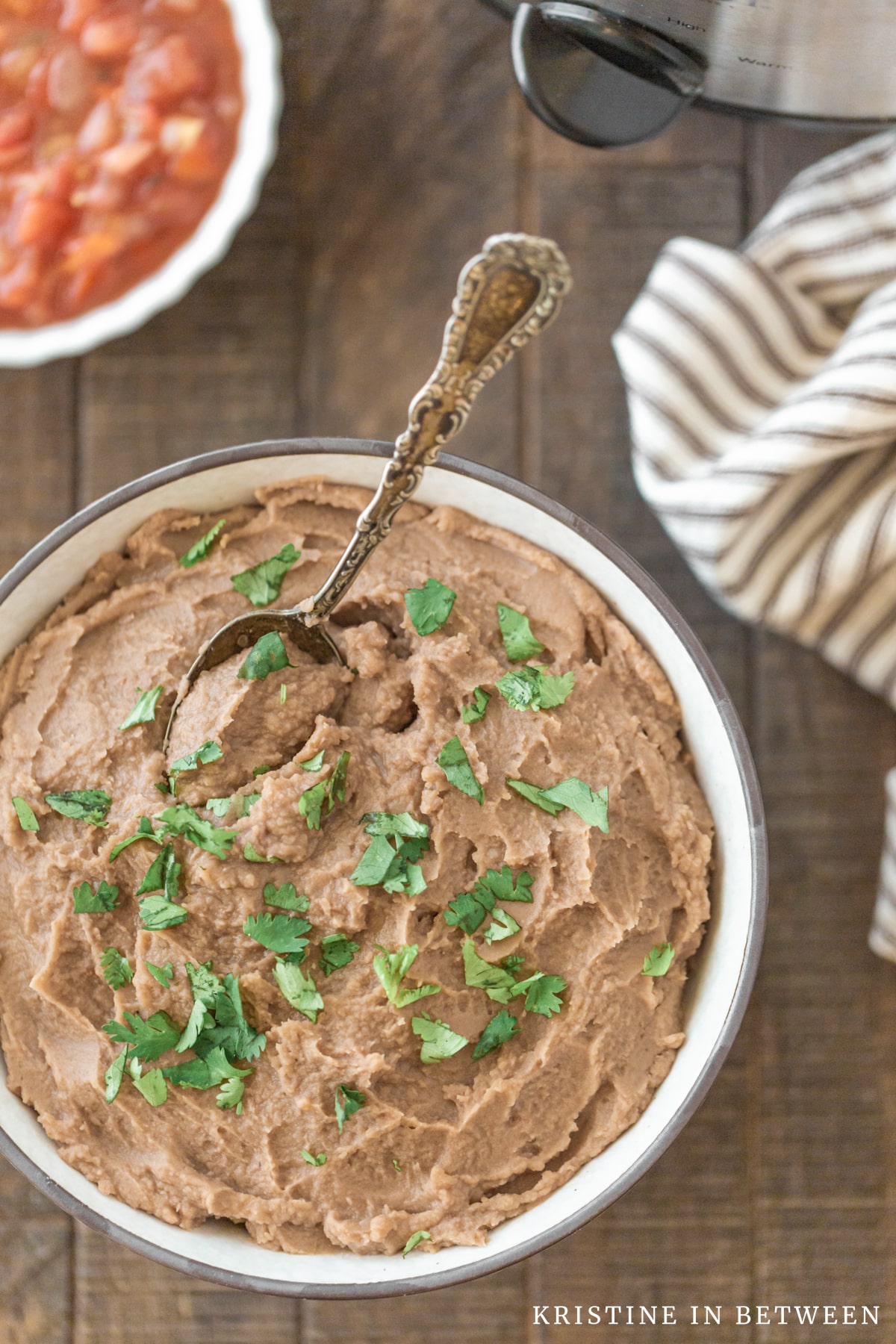 A bowl of refried beans sitting next to a Crock-pot and a small bowl of salsa.