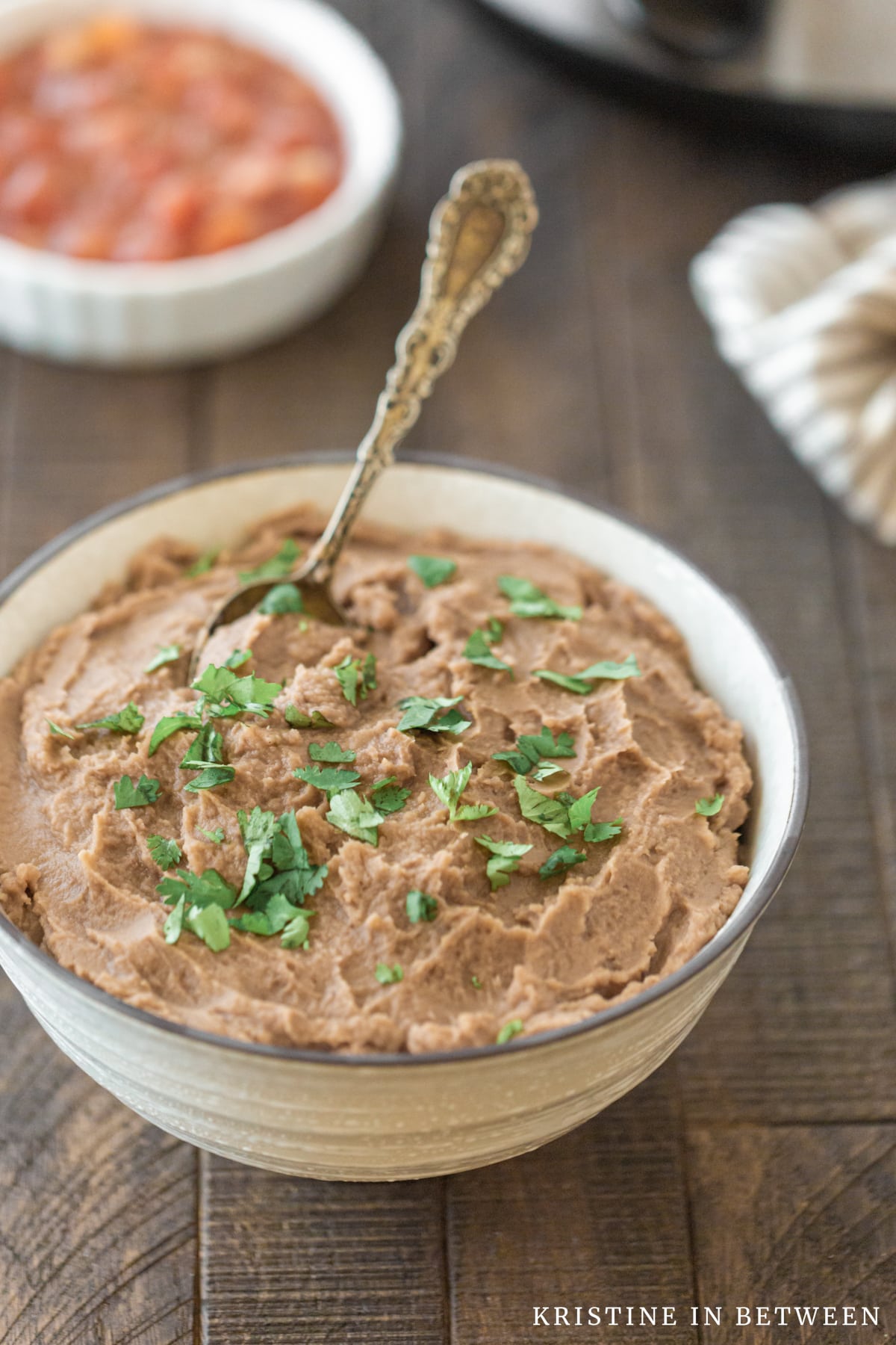 A bowl of refried beans sitting next to a Crock-pot and a small bowl of salsa.