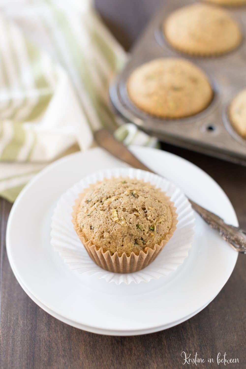 A single zucchini muffin sitting on a white plate with a small bread knife next to it.
