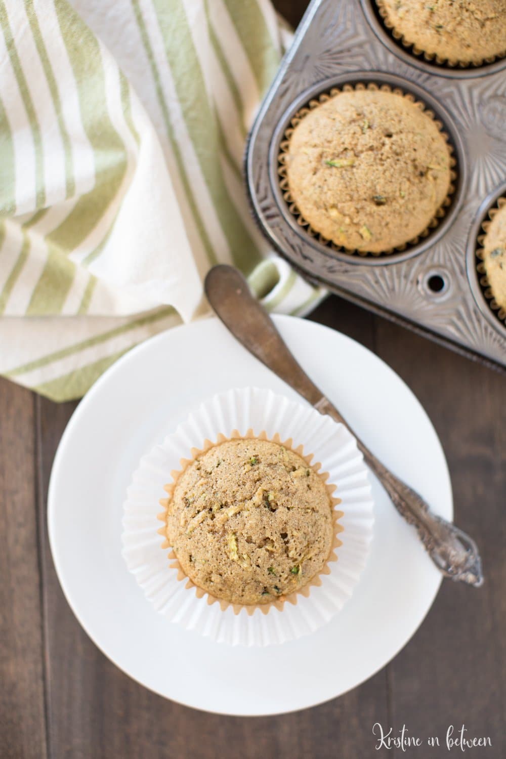 A zucchini muffin sitting on a white plate with a small knife and a green striped napkin in the background.