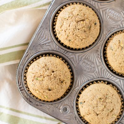 Whole what zucchini muffins in an antique muffin tin with a green striped napkin underneath them.