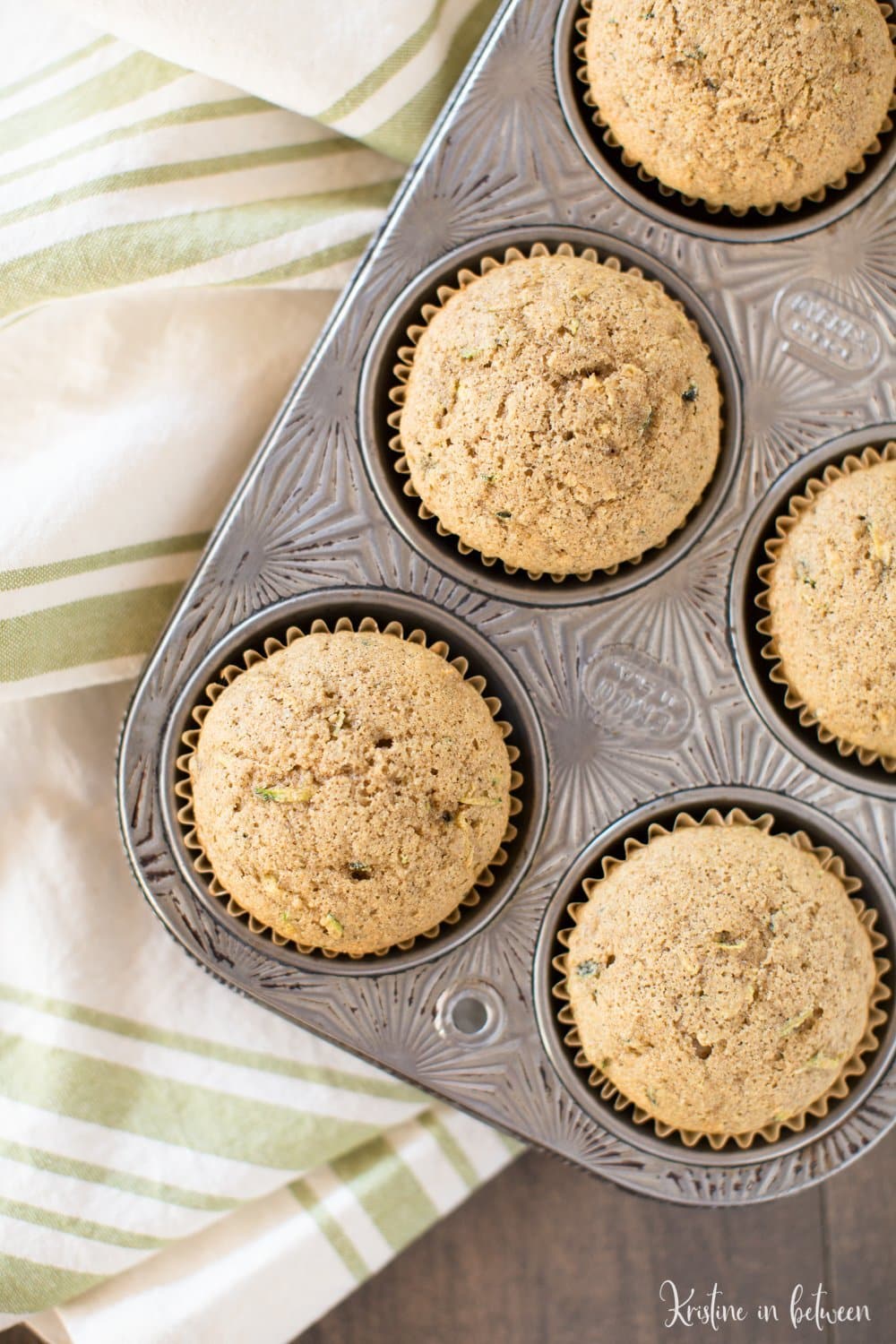 Whole what zucchini muffins in an antique muffin tin with a green striped napkin underneath them.