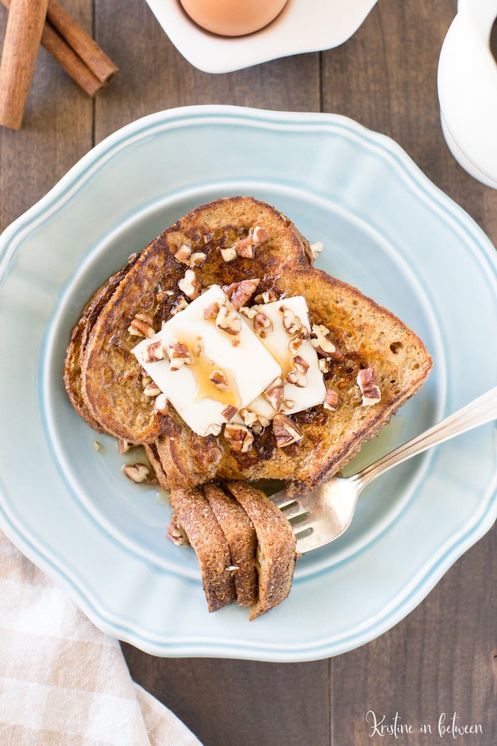 A light blue plate of French Toast with butter on top and a fork with a bite on it.