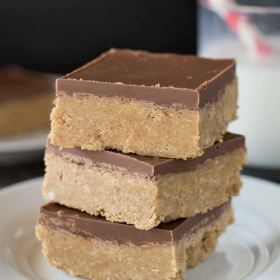 Chocolate peanut butter bars cut in squares, stacked up with a glass of milk in the background.