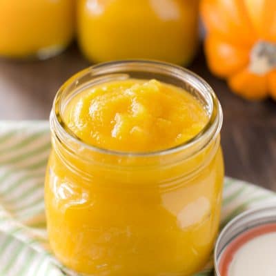 A jar of pumpkin puree sitting on a table with a sugar pumpkin.