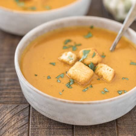A bowl of pumpkin soup with croutons on top and a spoon in it.