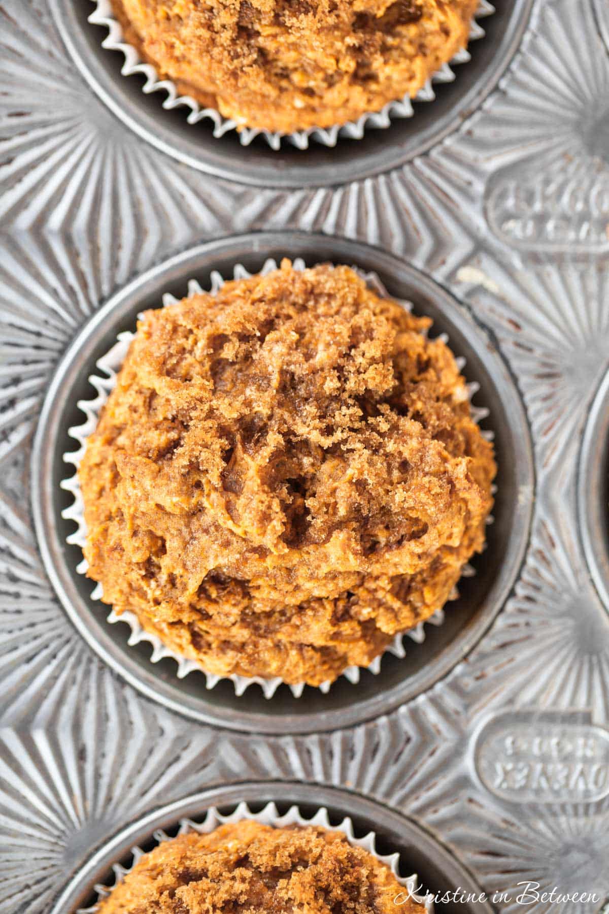 A closeup of the top of pumpkin muffins with crumb topping in an antique muffin tin.