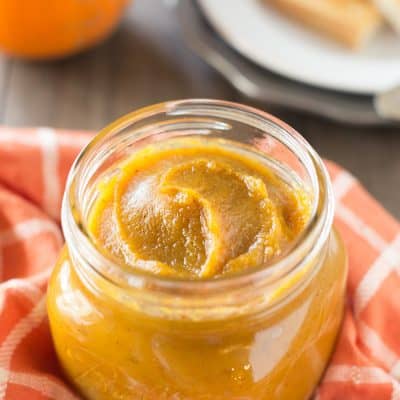 A jar of pumpkin butter sitting on a table with a sugar pumpkin.