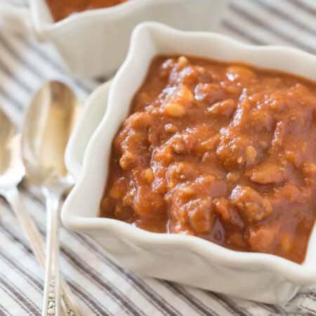 A bowl of pumpkin chili sitting with a spoon and a brown striped napkin.