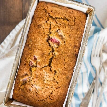 A loaf of strawberry banana bread in an antique loaf pan with two forks sitting next to it.
