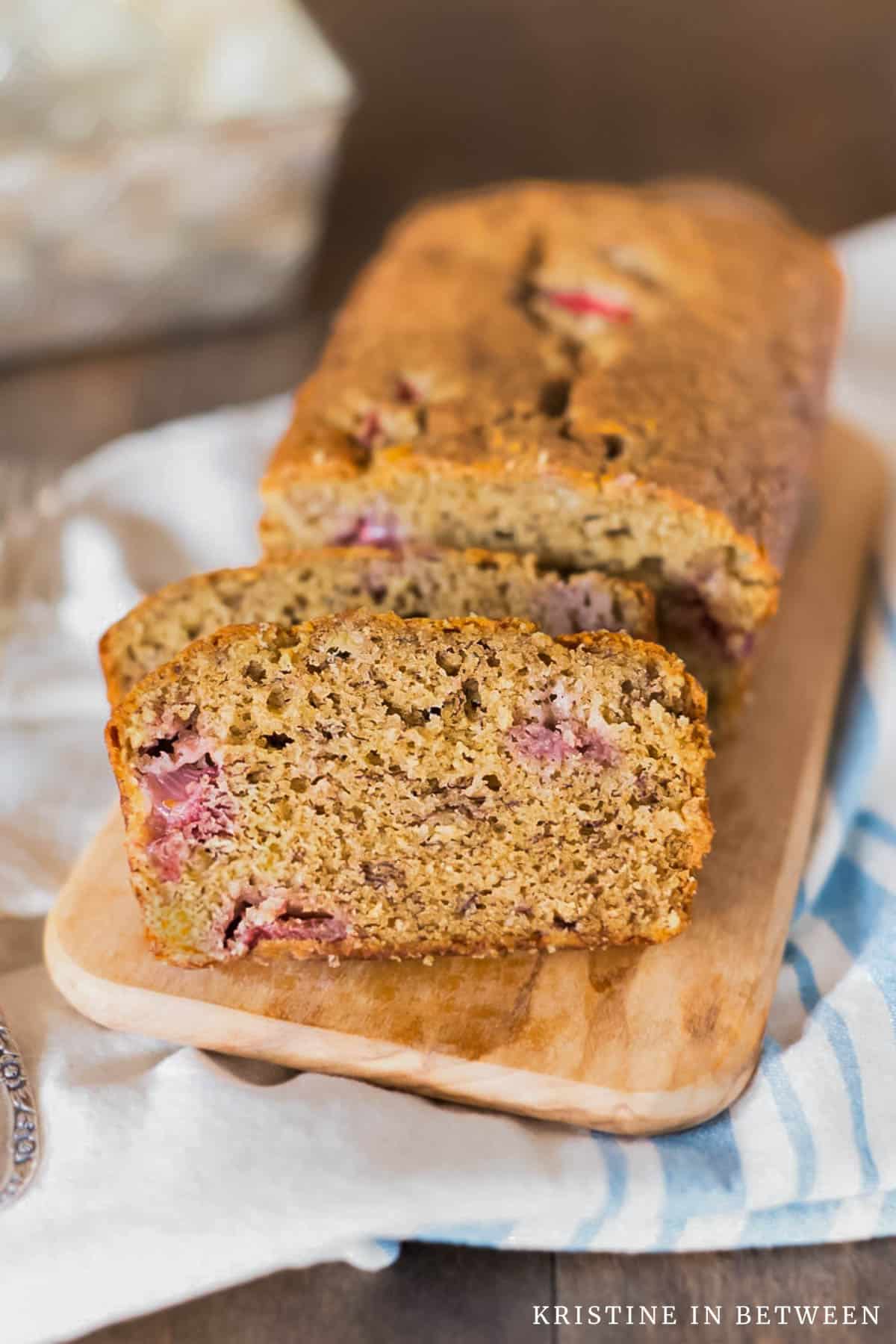 Slices of strawberry banana bread on a wooden board with the rest of the loaf in the background.