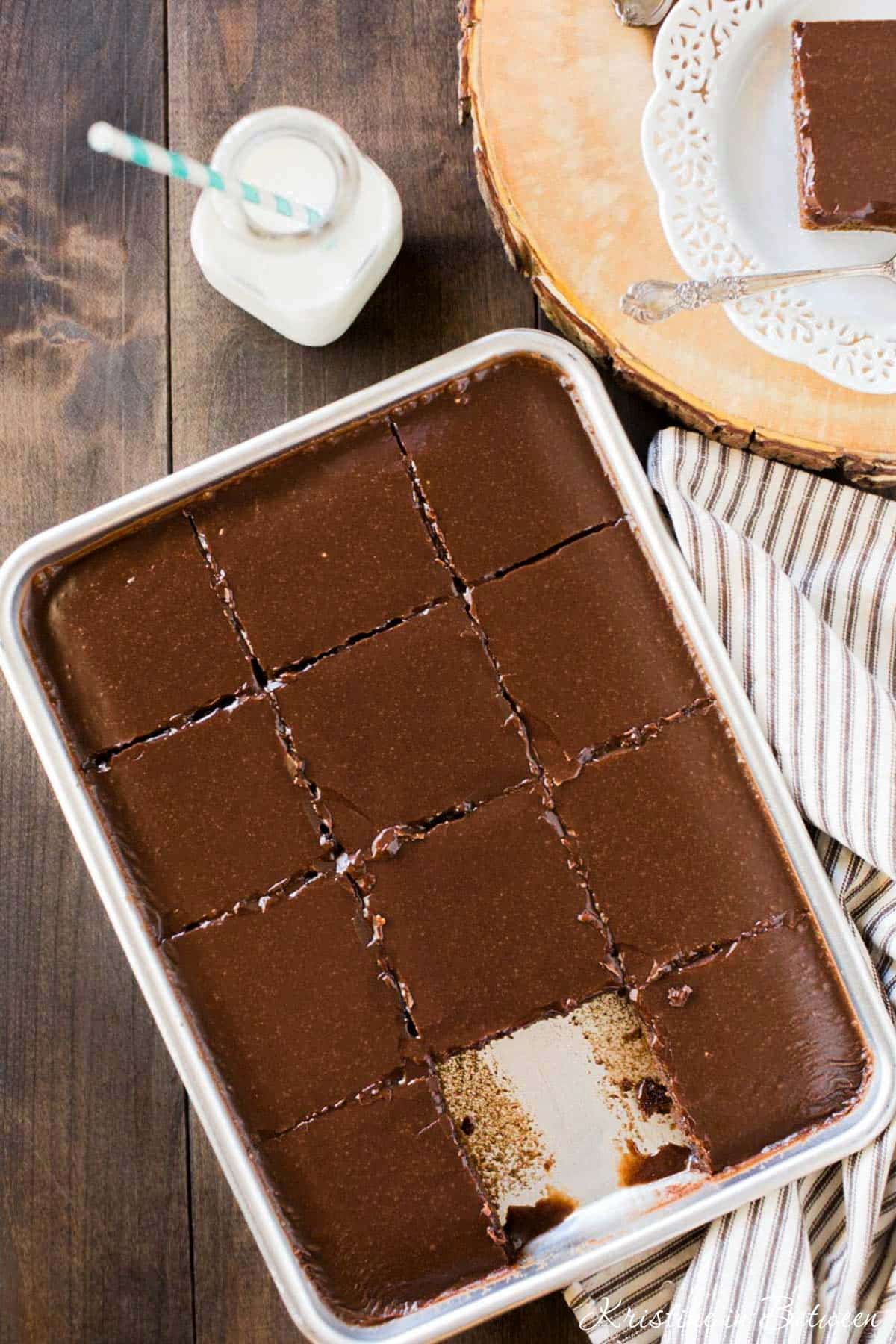 A freshly baked and frosted Texas sheet cake in a small sheet pan with a jar of milk sitting next to it.
