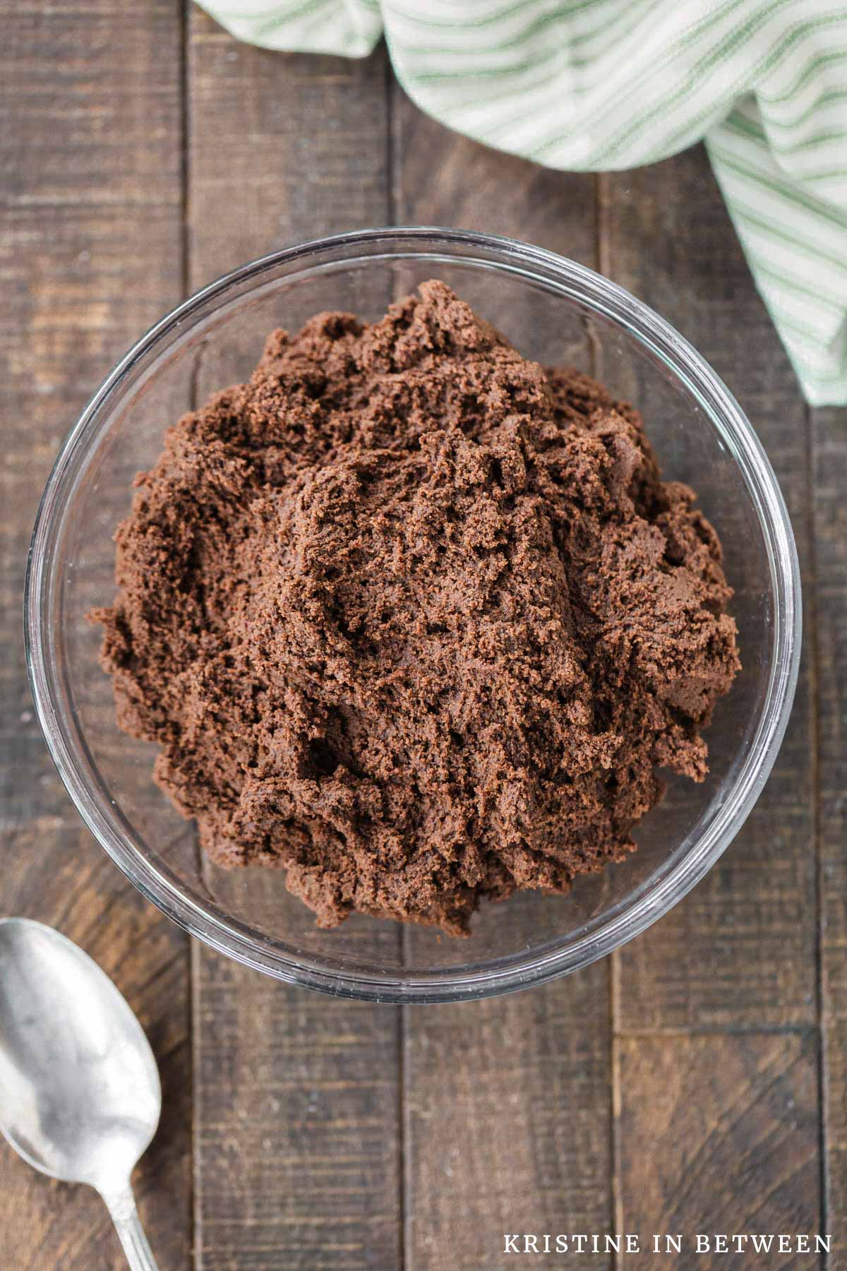 A glass bowl of chocolate cookie dough with a spoon sitting next to it.