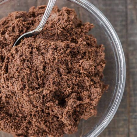 A glass bowl of chocolate cookie dough with a spoon in it.