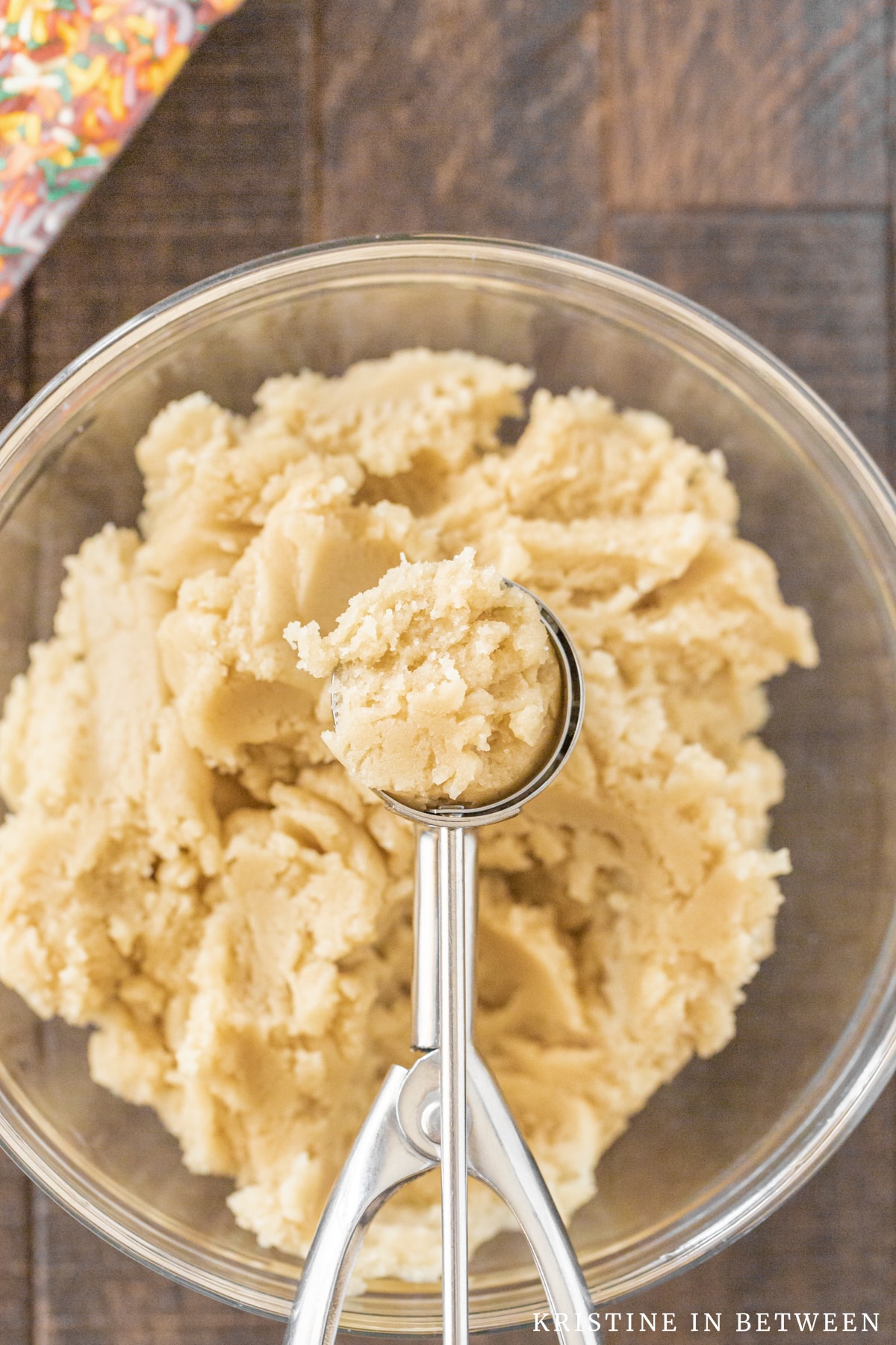 A bowl of cookie dough with a scoop laying on top and sprinkles in the background.