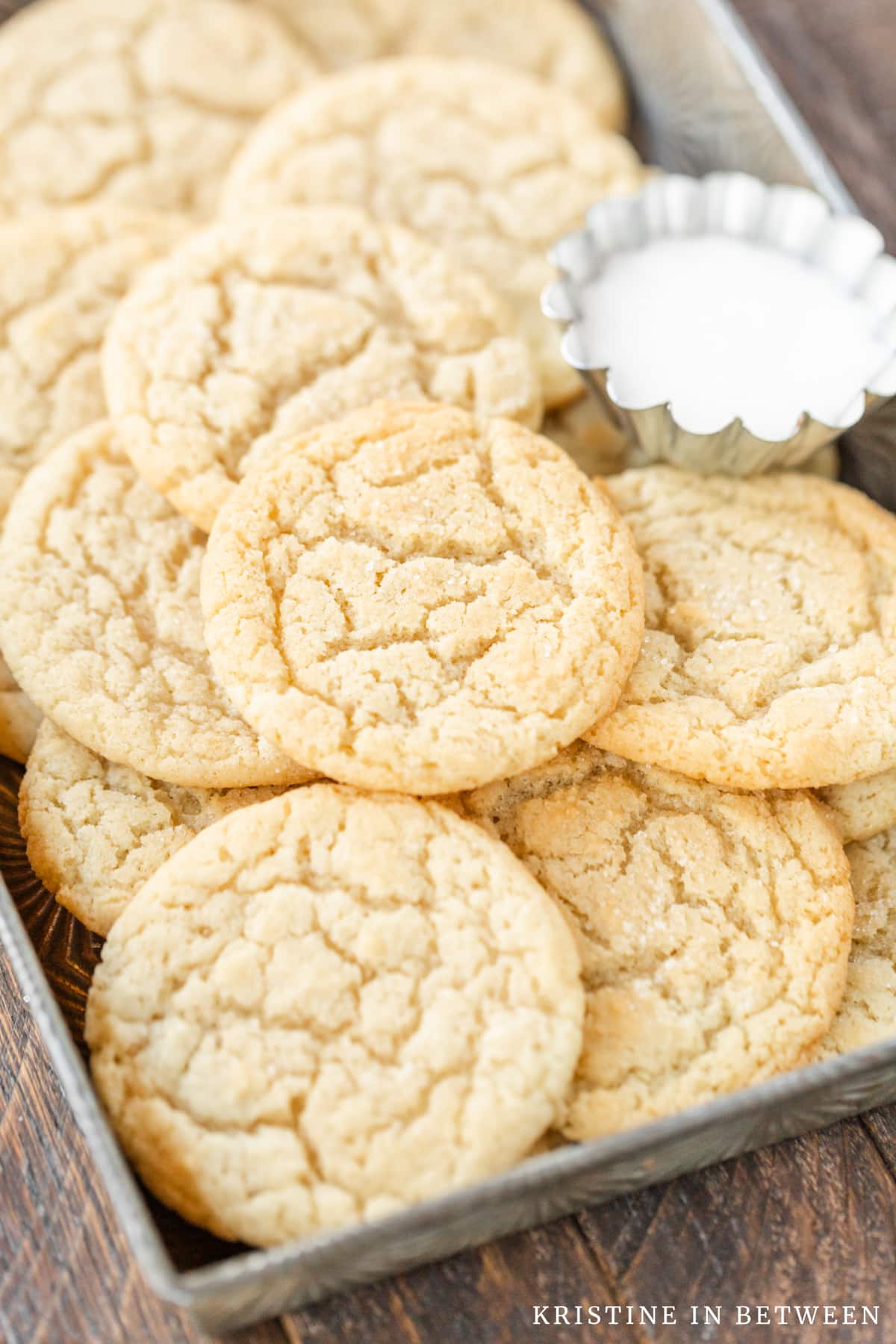 A stack of sugar cookies with a bowl of sugar sitting next to them.
