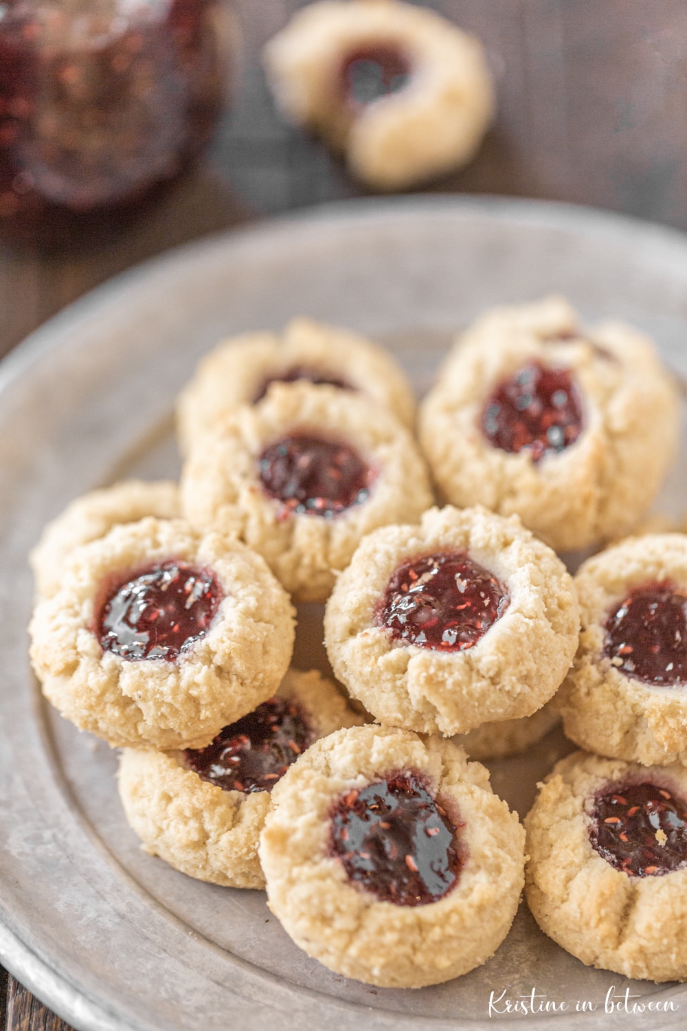 Shortbread cookies sitting on a tin plate with a jar of jam in the background.