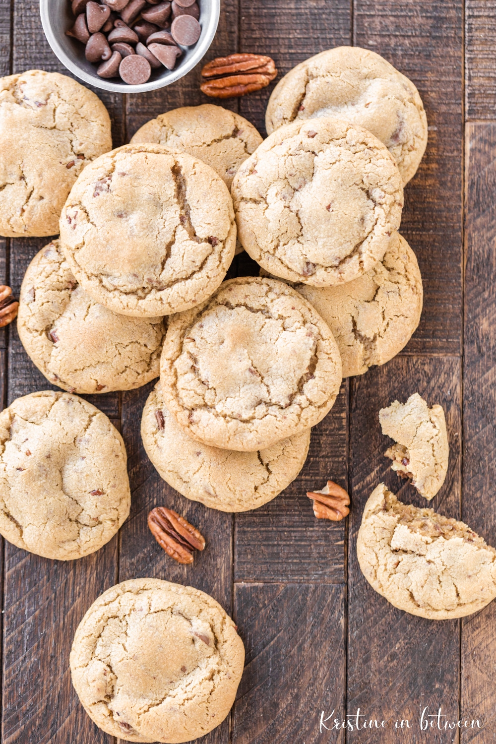 A pretty stack of cookies spread out on a dark wooden board with pecans scattered