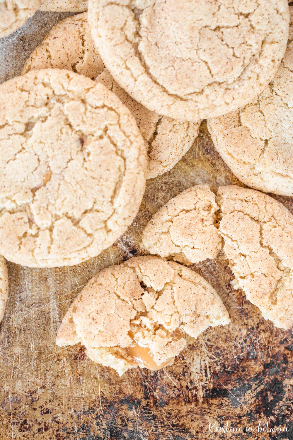 A cookie broken in half laying on a baking sheet with caramel seeping out.
