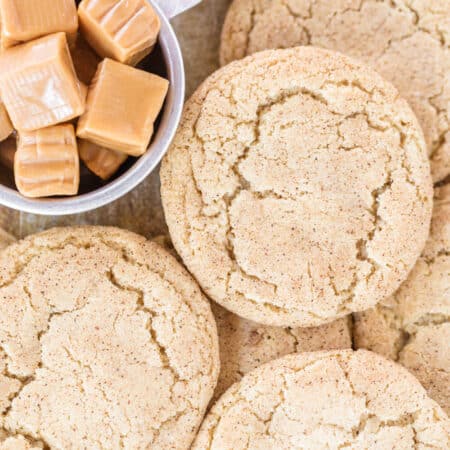 Cookies piled up on a cookie sheet with a small bowl of caramels.