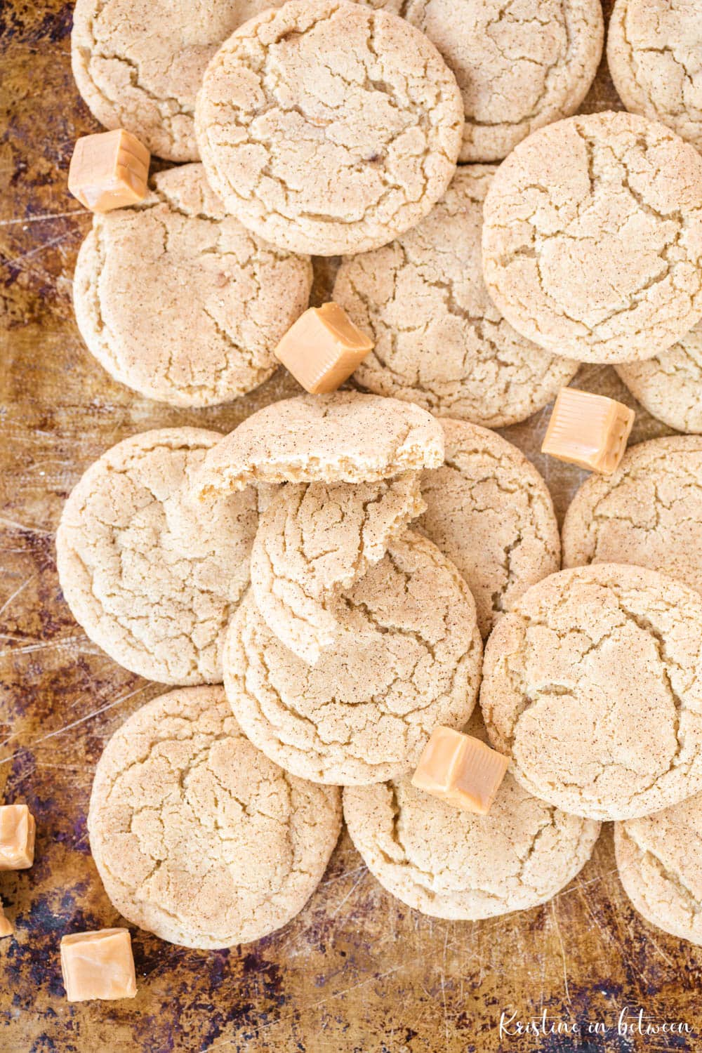 Cookies laying on a baking sheet with caramel candies sprinkled in between.