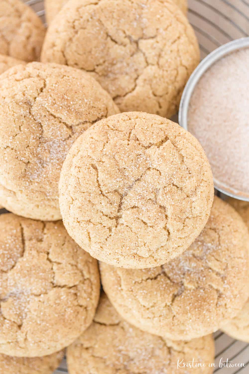 Cookies piled up on a wire rack with a small bowl of cinnamon and sugar.