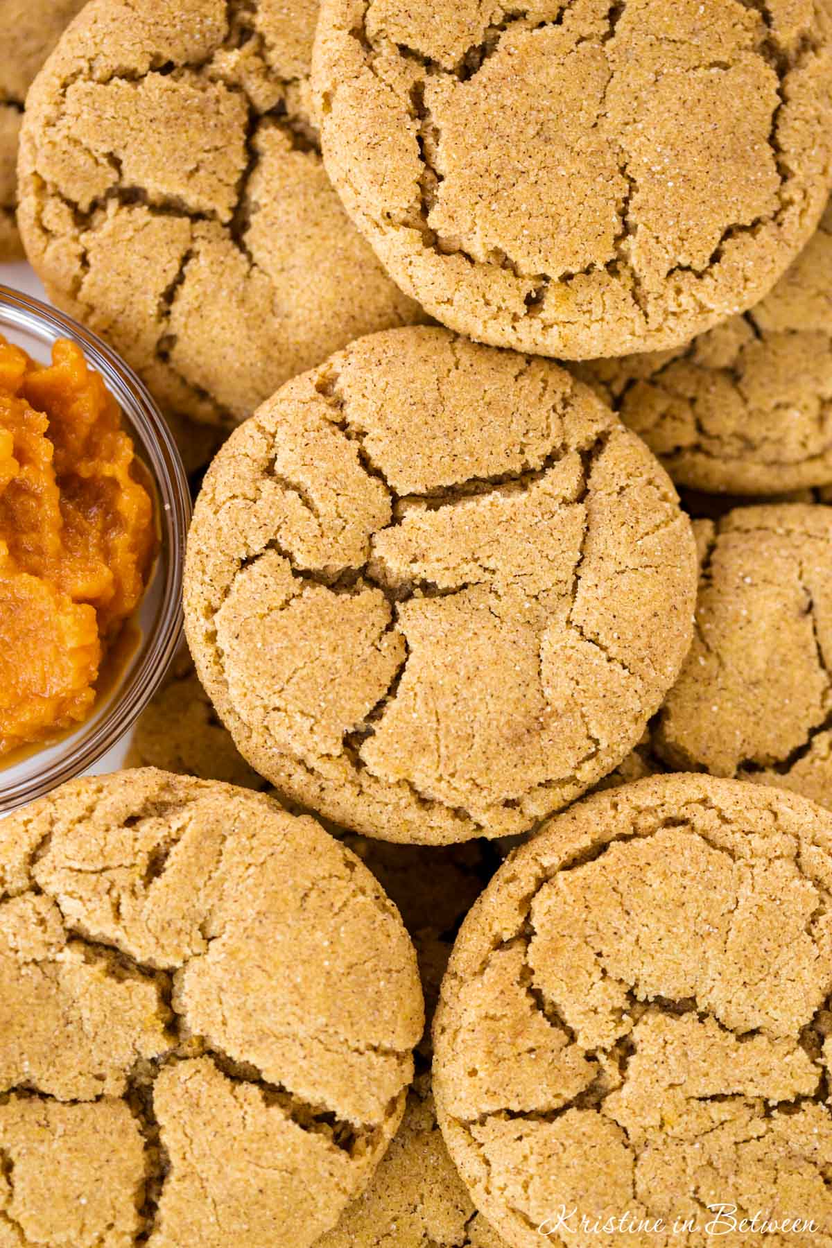Pumpkin snickerdoodle cookies laying on a white tray with a small bowl of pumpkin puree next to them.