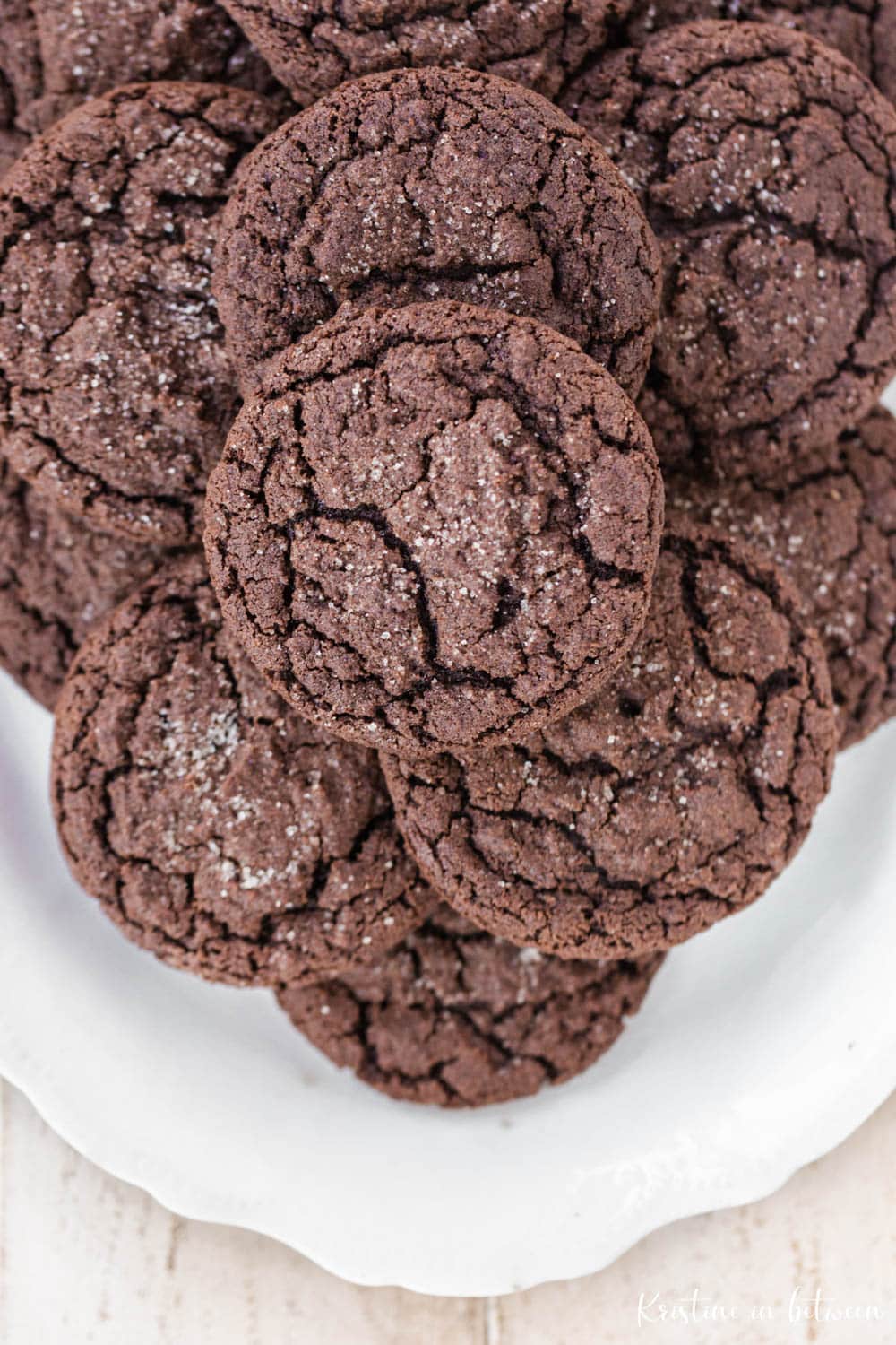 Chocolate cookies laying on a white scalloped edge platter.