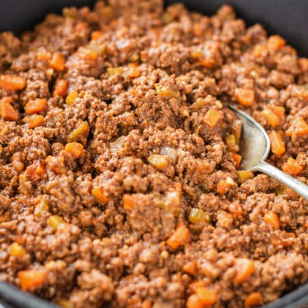 Cooked Sloppy Joes sitting in a cast iron pan with an antique spoon in it.