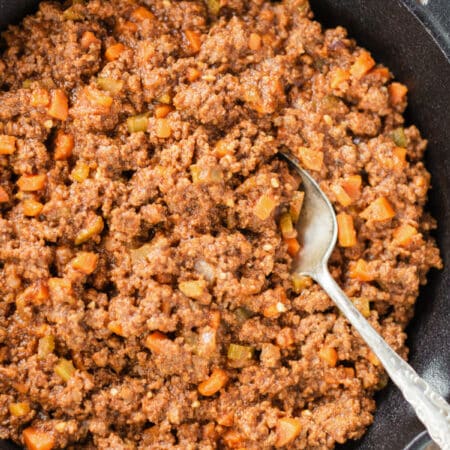 Cooked Sloppy Joes sitting in a cast iron pan with an antique spoon in it.