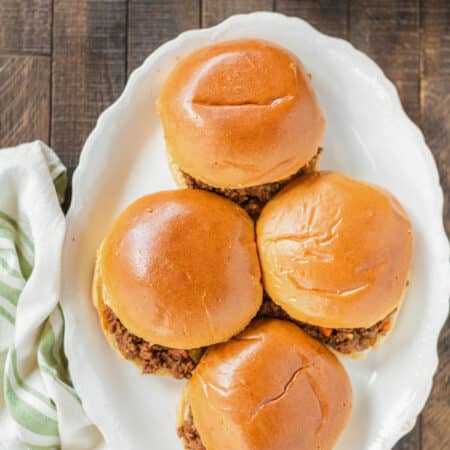 Sloppy Joes sitting on a white platter with a green napkin sitting next to them.