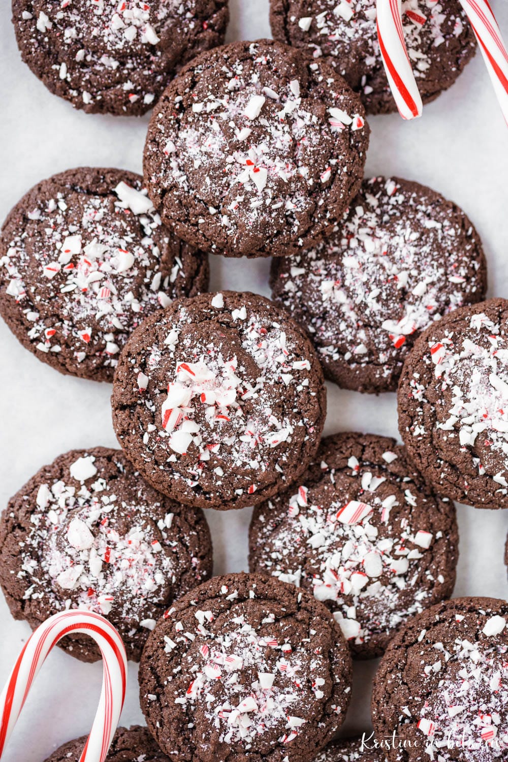 Cookies dusted with crushed peppermint laying on parchment paper with a candy cane next to them.