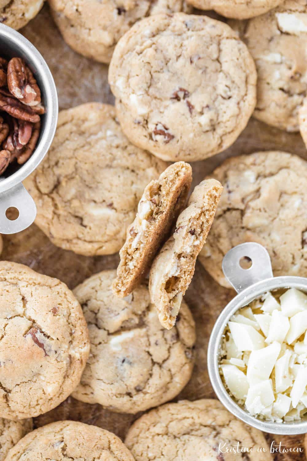 A cookie broken in half to show the inside texture piled up on cookies laying on a cookie sheet.
