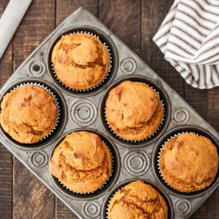 Pumpkin muffins in a muffin tin with a striped napkin and a knife next to them.