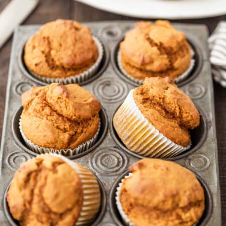 Pumpkin muffins in a muffin tin with a striped napkin and a knife next to them.