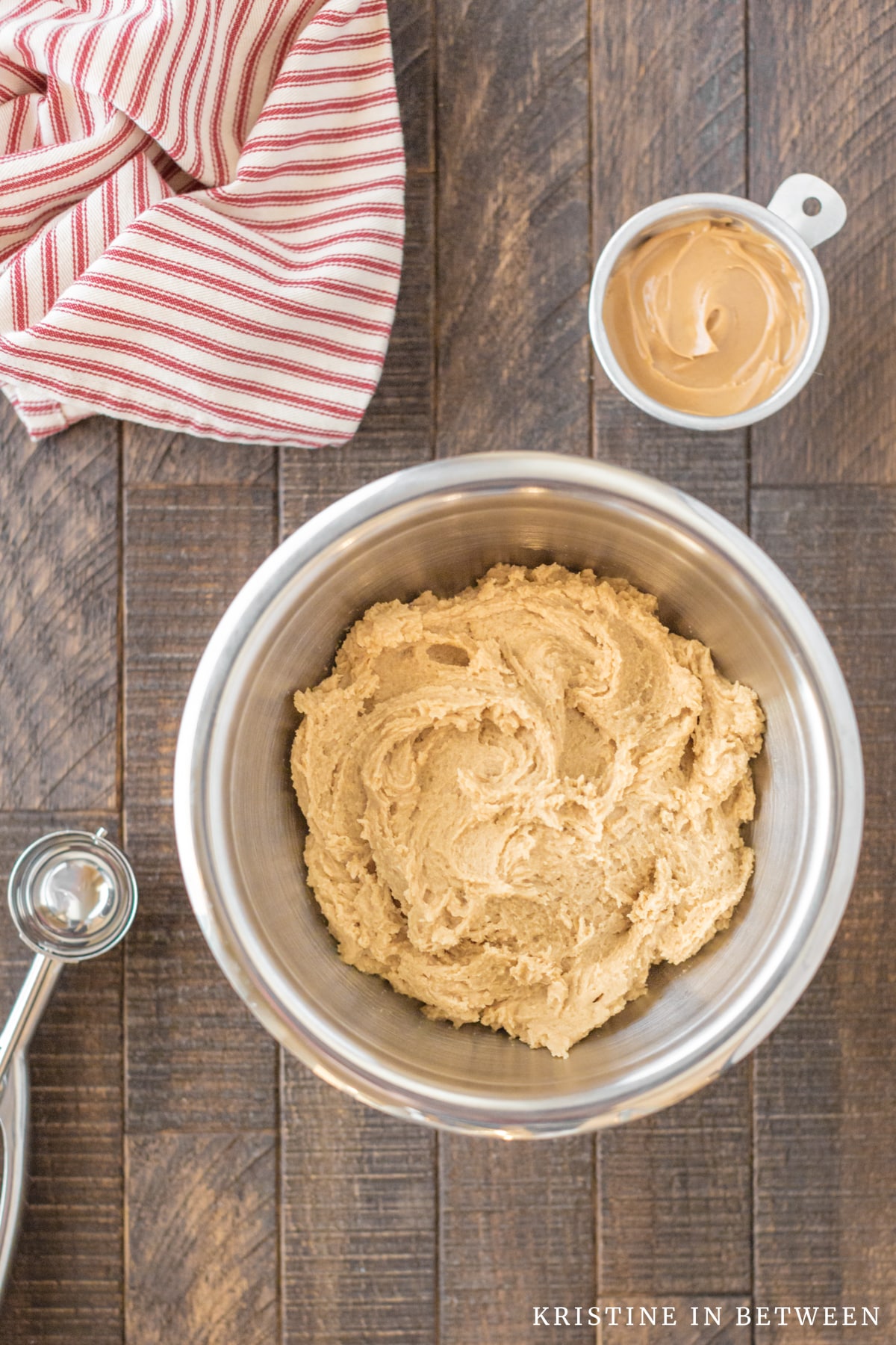 A bowl of peanut butter cookie dough with a cookie scoop and a small bowl of peanut butter sitting next to it.