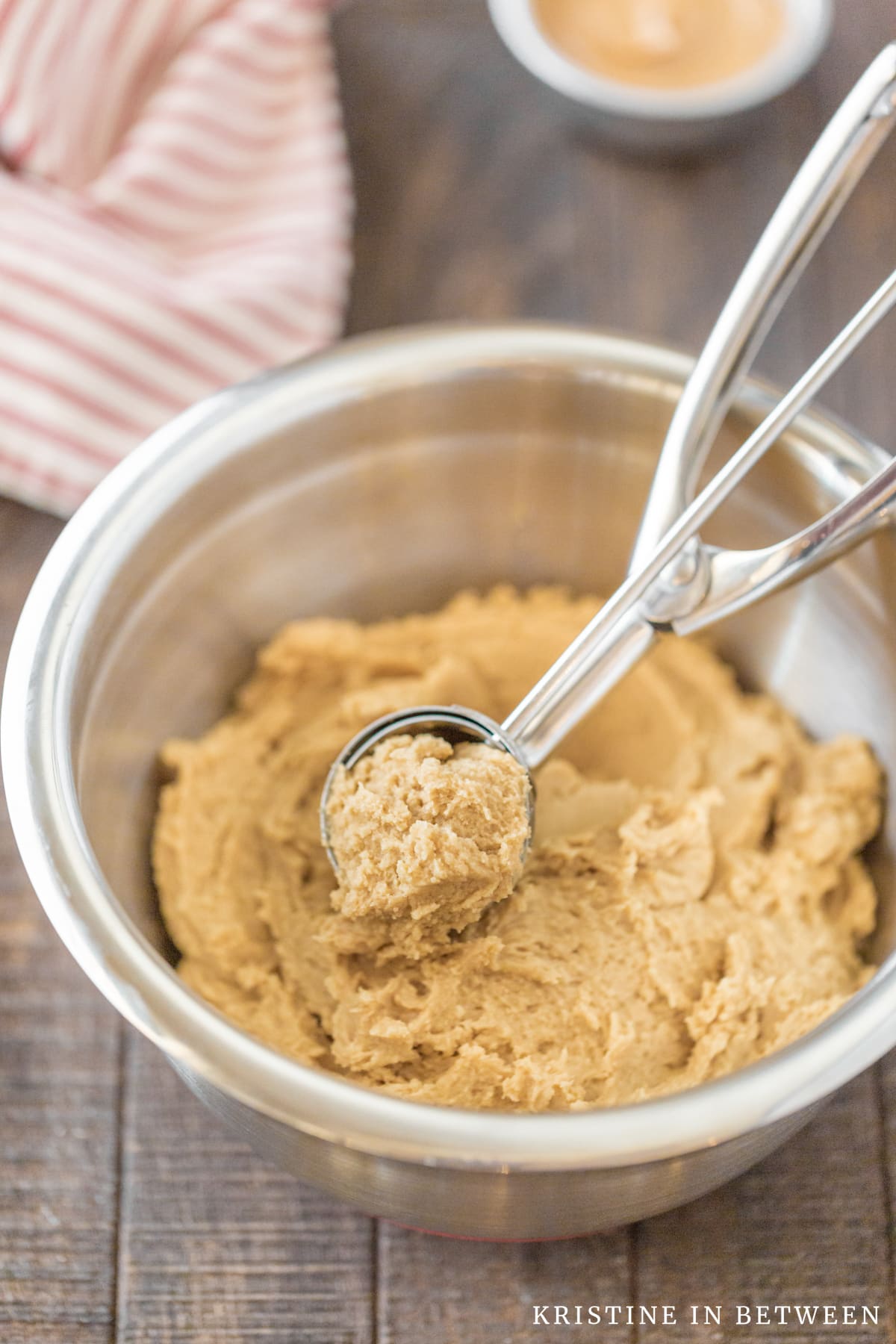 A bowl of peanut butter cookie dough with a cookie scoop in it and a small bowl of peanut butter sitting next to it.