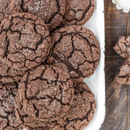 Cookies stacked up on a white tray with a small bowl of sugar sitting next to them.
