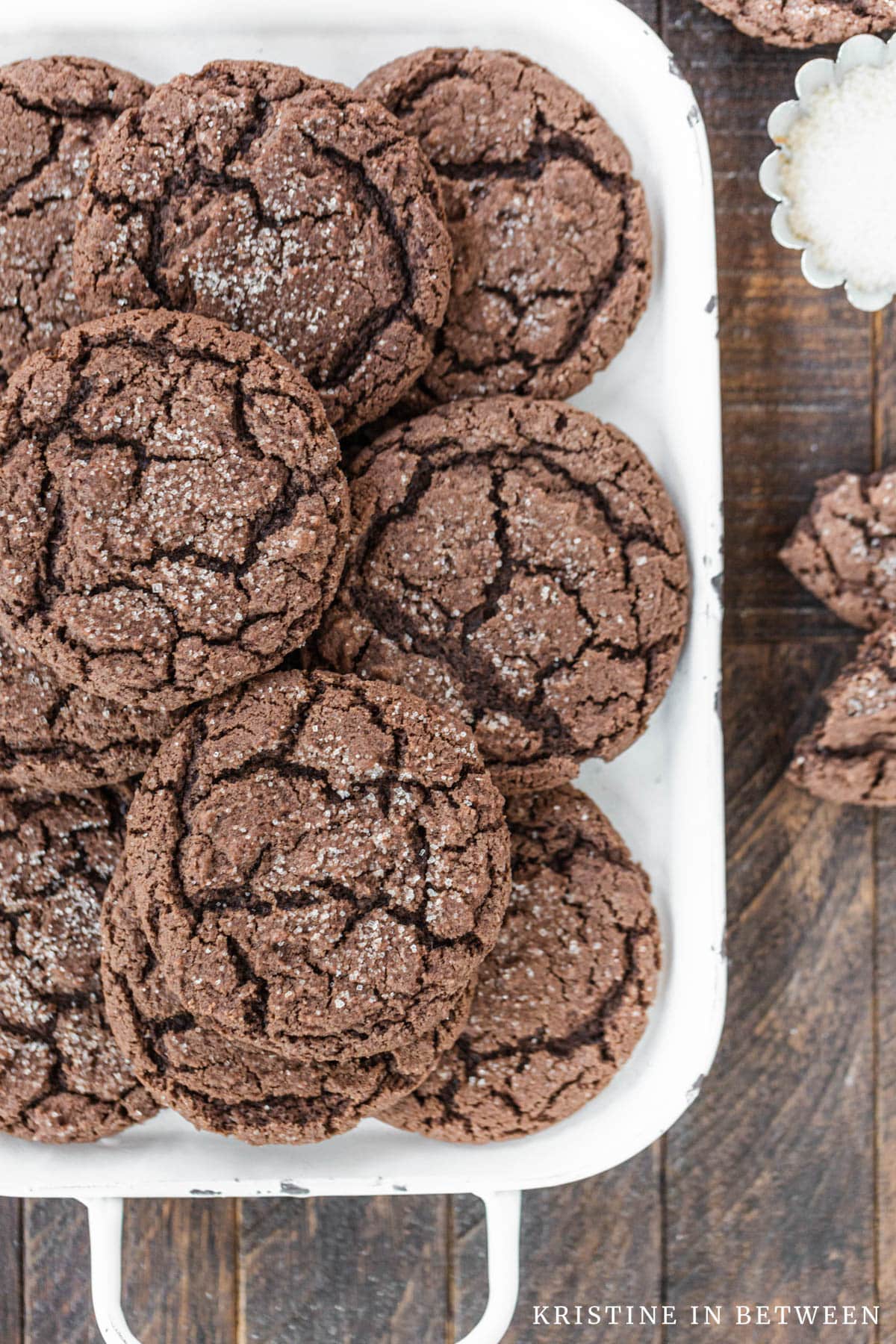 Cookies stacked up on a white tray with a small bowl of sugar sitting next to them.