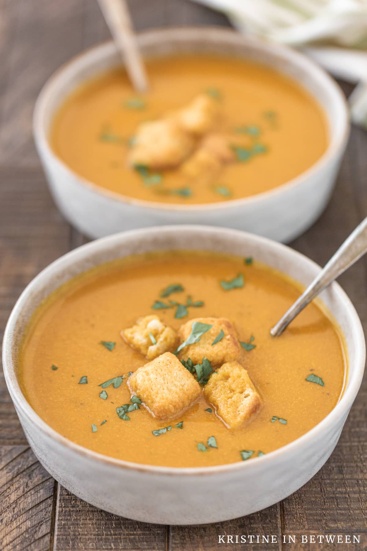 A bowl of pumpkin soup with croutons on top and a spoon in it.