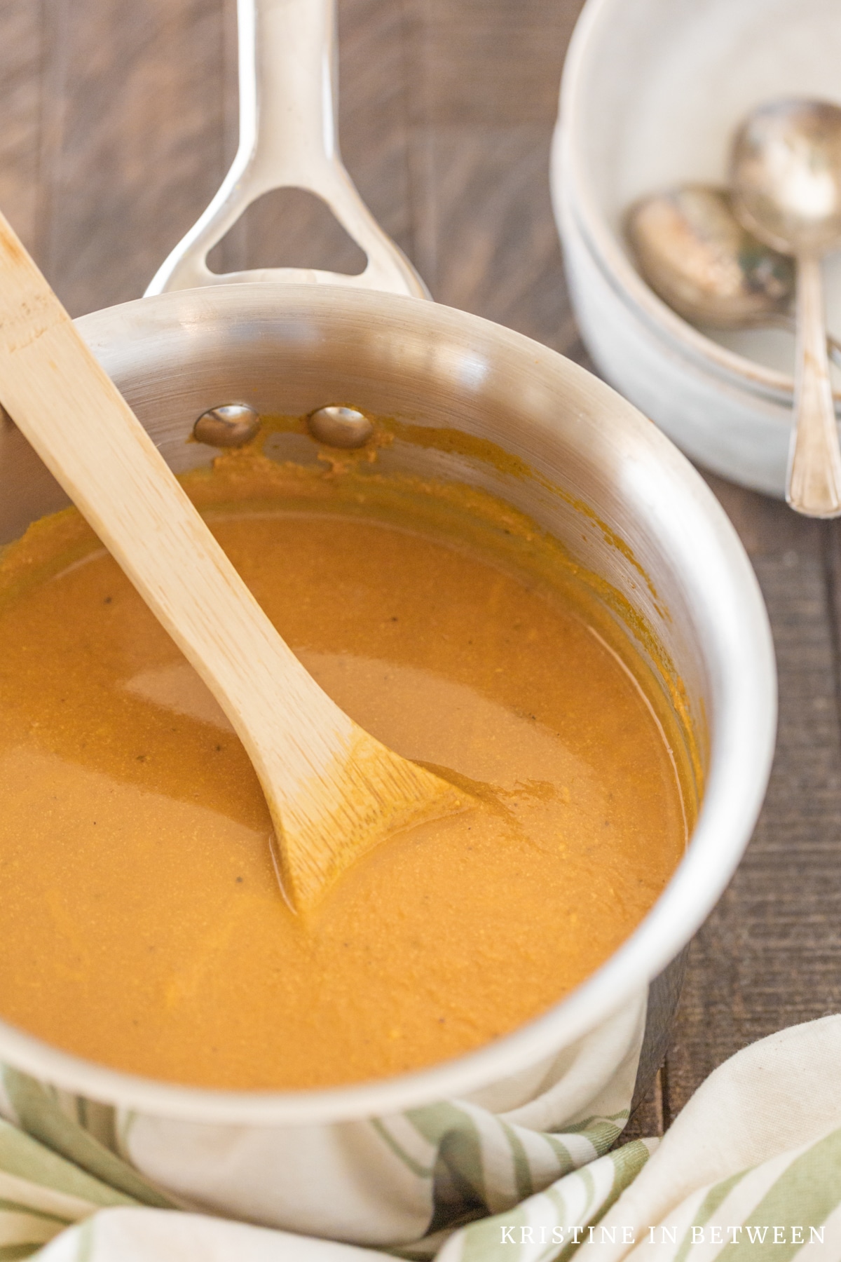 Pumpkin soup in a saucepan with a wooden spoon in it.