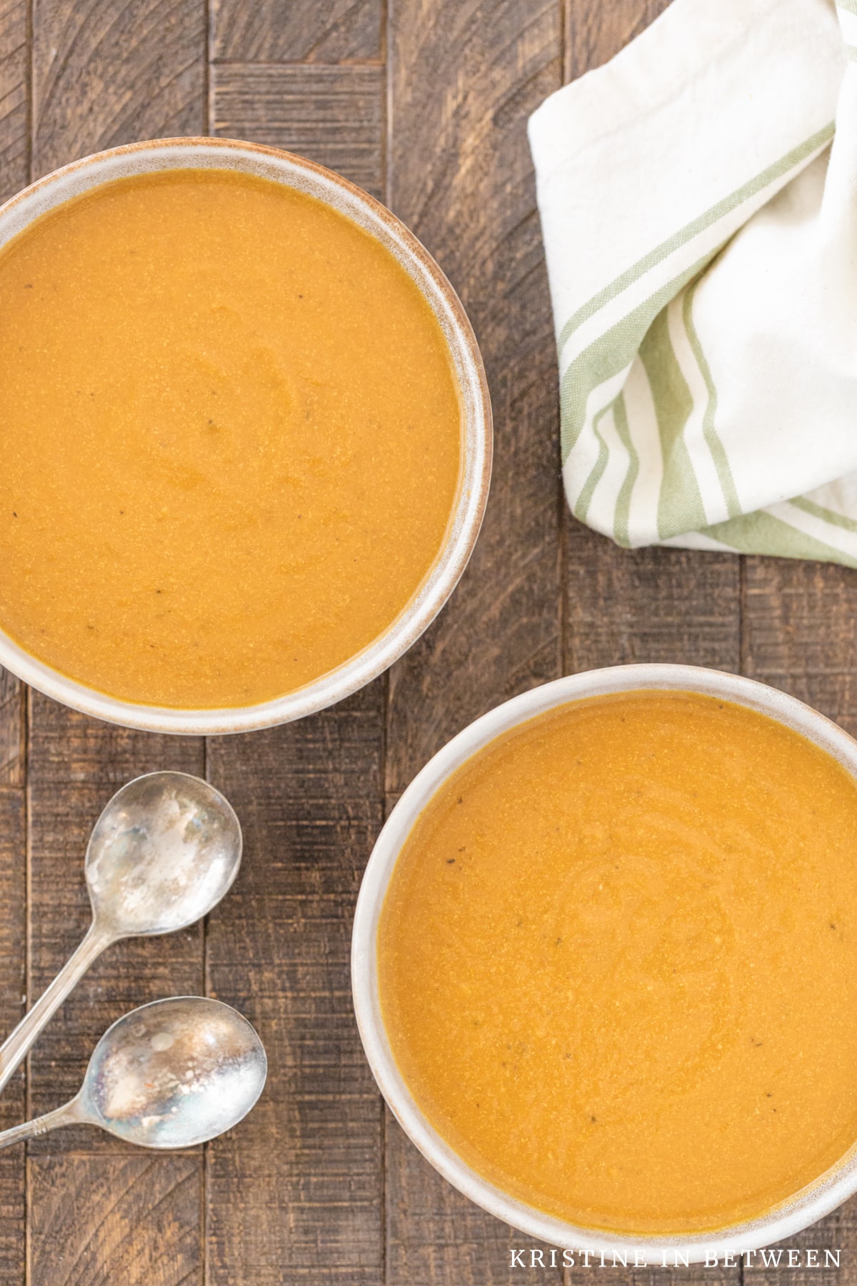 Two bowls of pumpkin soup sitting with two spoons and a green striped napkin.