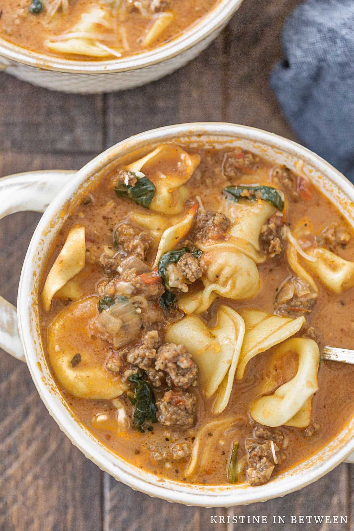 A bowl of tortellini soup with a blue napkin in the background.