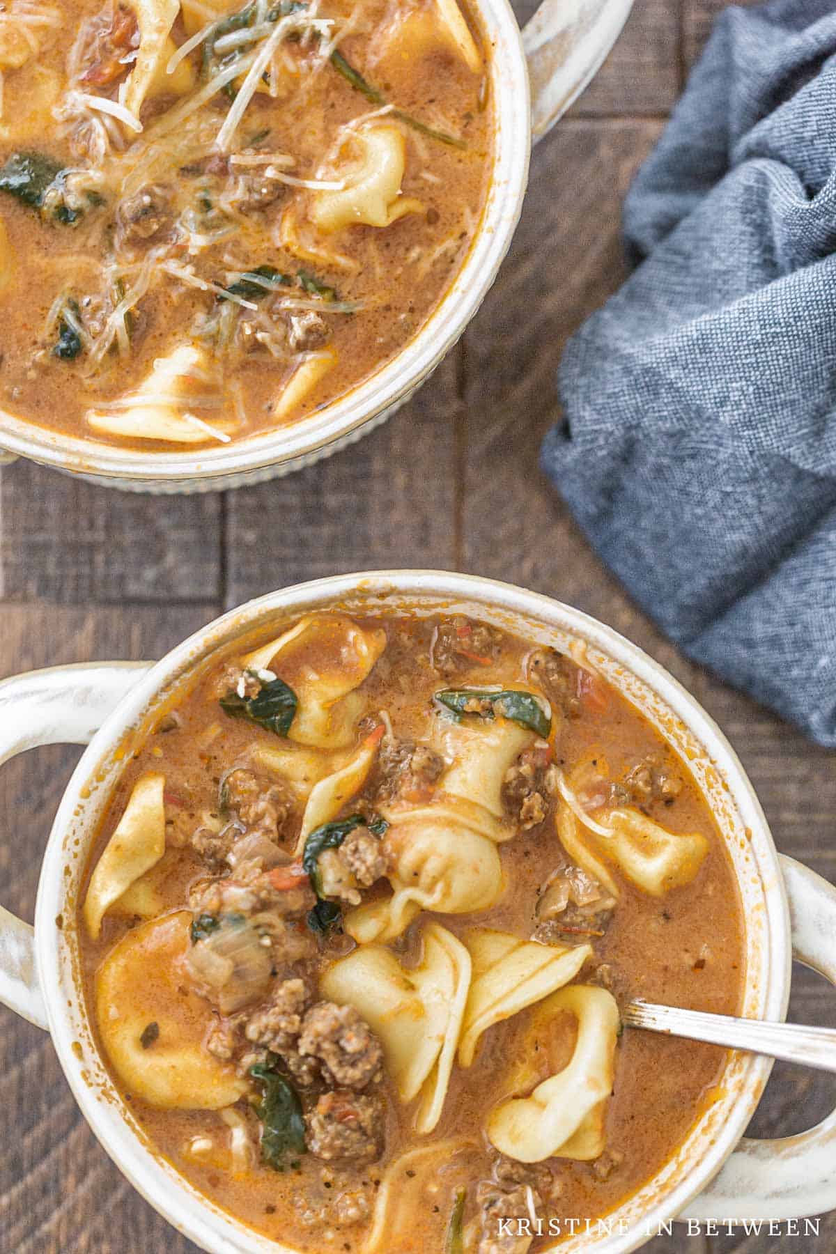 Two bowls of soup with spoons in them and a blue napkin laying next to them.