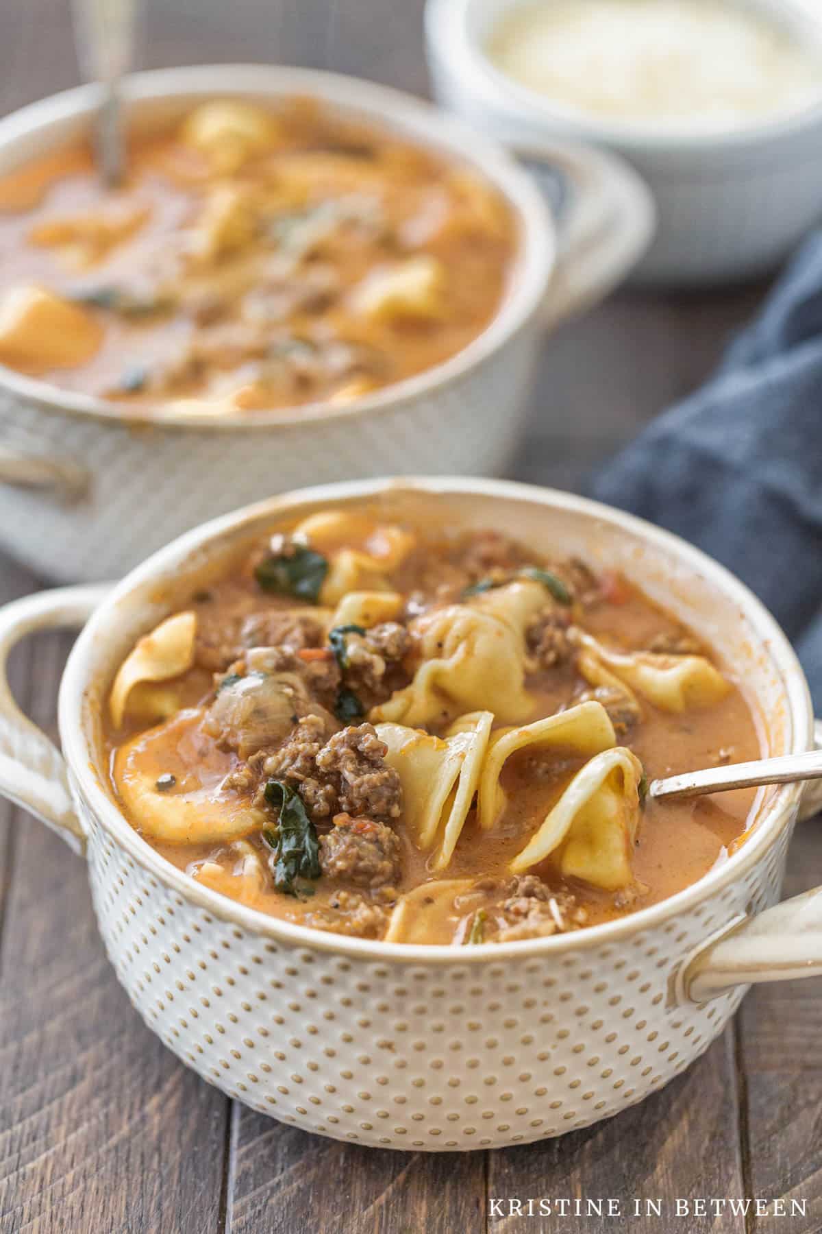 Two bowls of soup with spoons in them and a blue napkin laying next to them.